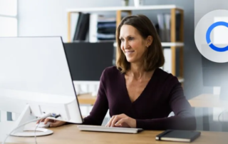 Mujer mira a un ordenador de sobremesa de forma sonriente. Está utilizando los add-ons de Sage 200
