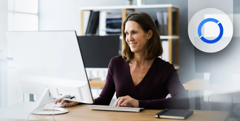 Mujer mira a un ordenador de sobremesa de forma sonriente. Está utilizando los add-ons de Sage 200
